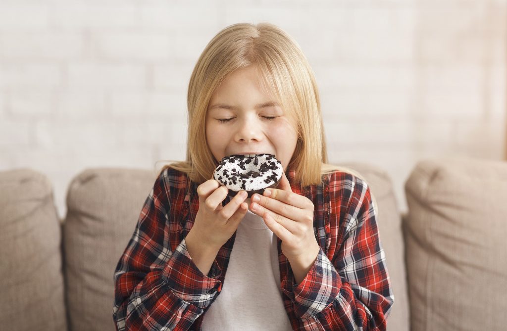 saúde oral: menina a comer um donut em casa